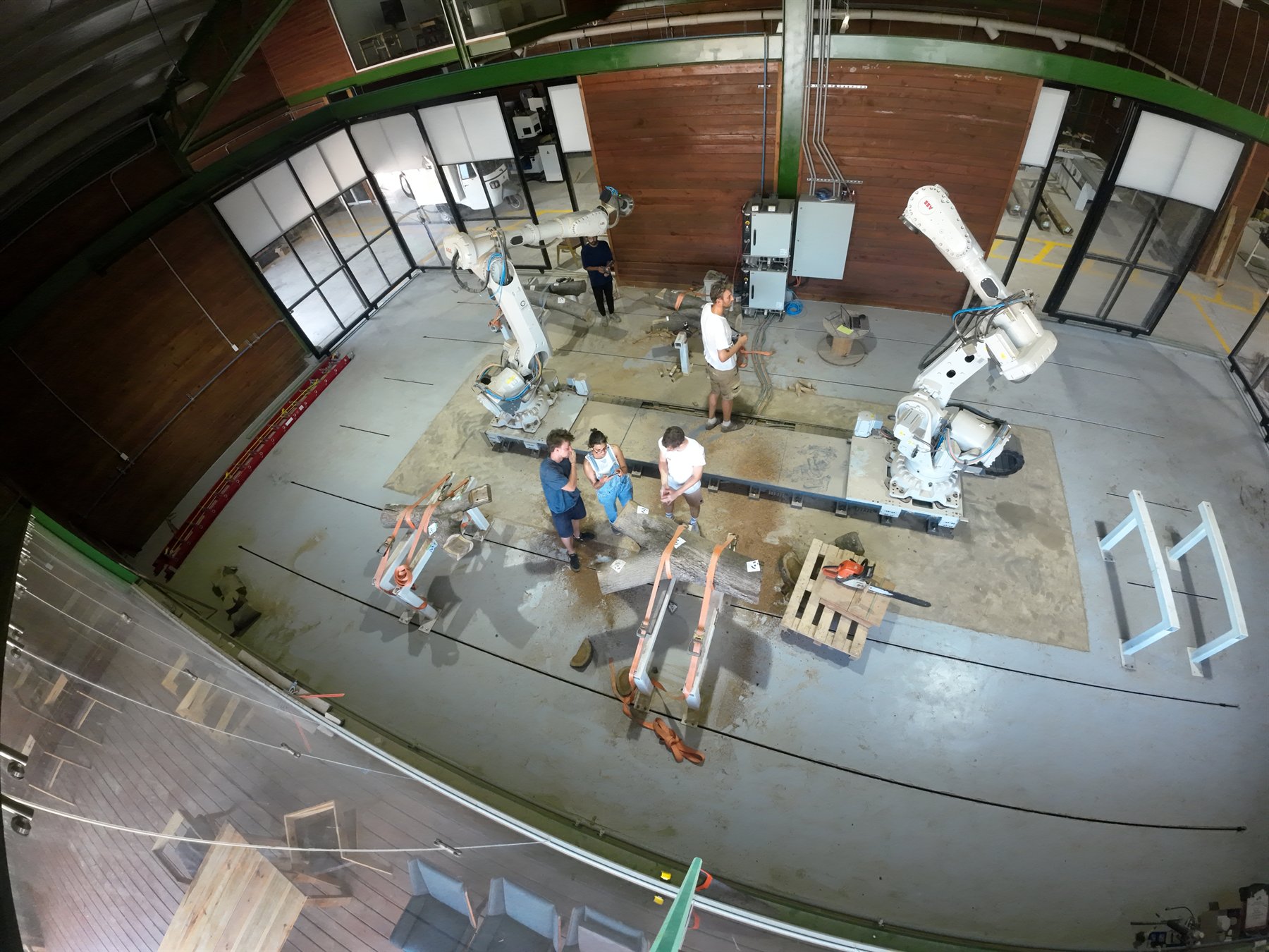 Overhead robotics workshop view with participants and two industrial robots.
